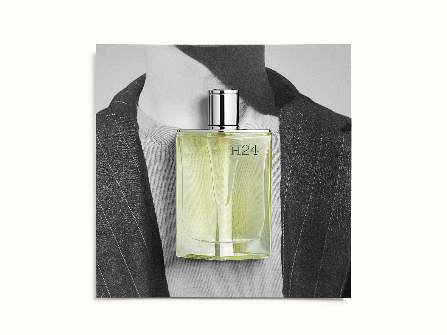 El frasco de perfume H24 tiene un líquido amarillo verdoso, con un tapón plateado, sobre un fondo en blanco y negro de un hombre con traje.
