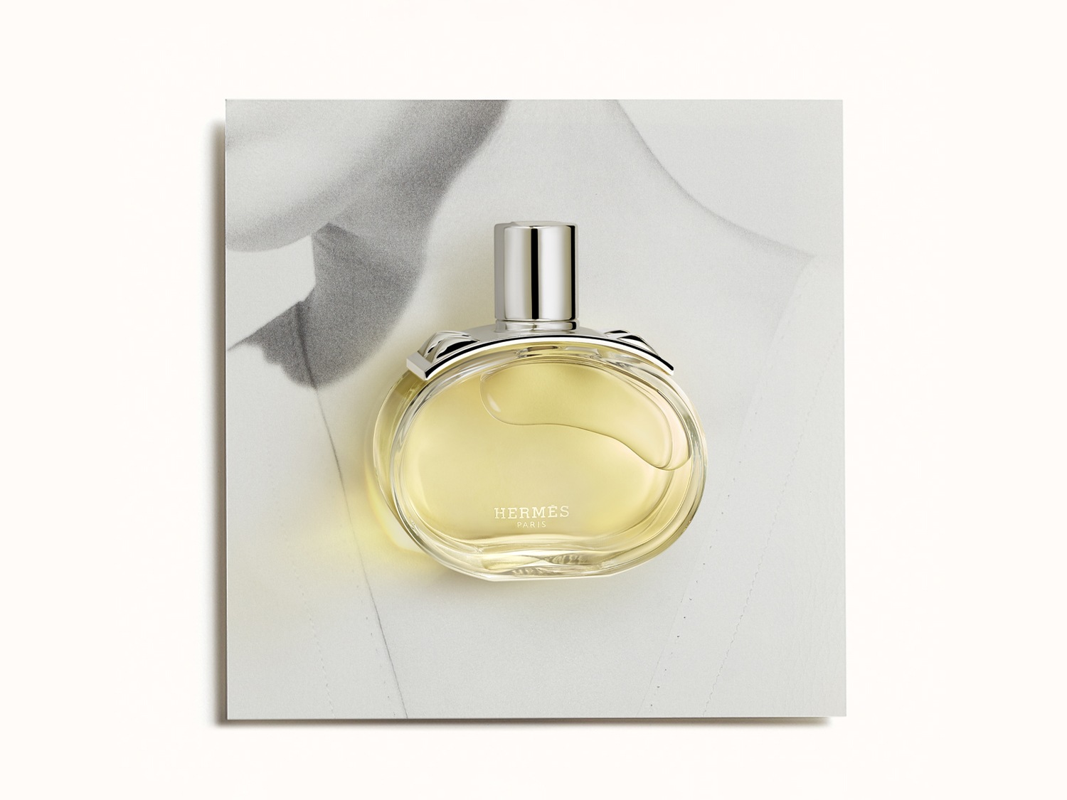 El frasco redondo de perfume Hermès, con su líquido amarillo pálido y tapón plateado, evoca una sensación de lujo y sofisticación.