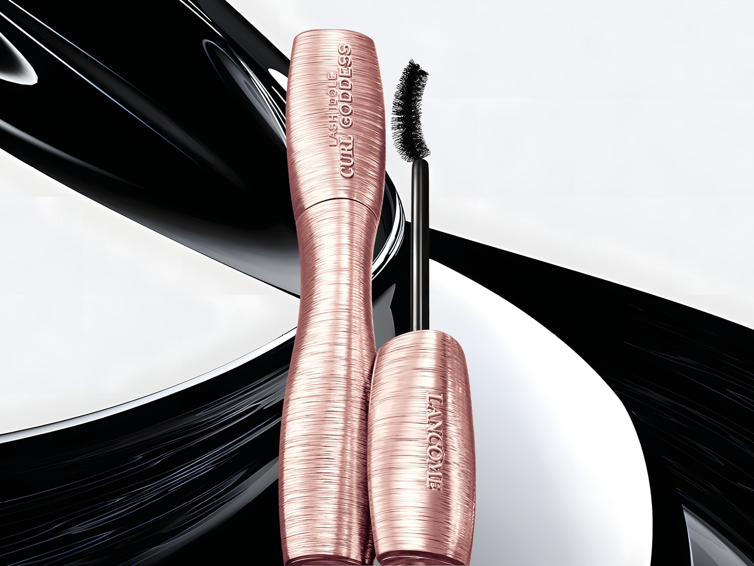 El rímel Lancôme Lash Idôle Curl Goddess en un envase de oro rosa texturizado, con el cepillo abierto mostrando sus cerdas negras, se presenta sobre un fondo abstracto blanco y negro.