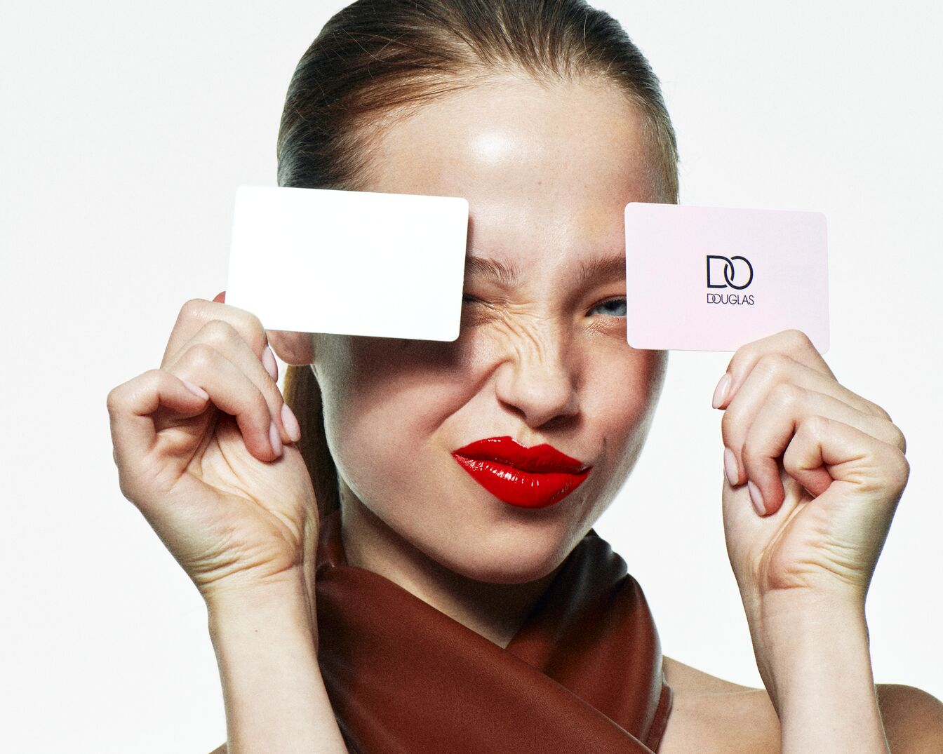 Eine Frau mit roten Lippen hält eine weiße Karte vor einem Auge und eine Douglas-Karte vor dem anderen.