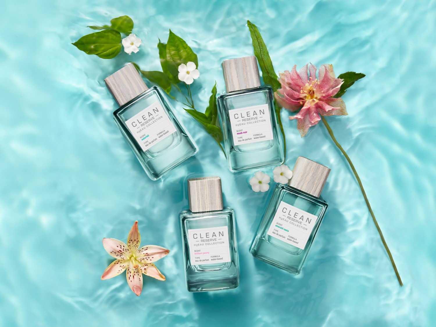 Cztery flakony perfum Clean Reserve H2Eau Collection w odcieniach błękitu, otoczone kwiatami i liśćmi, unoszą się na wodzie, tworząc świeżą i naturalną kompozycję.