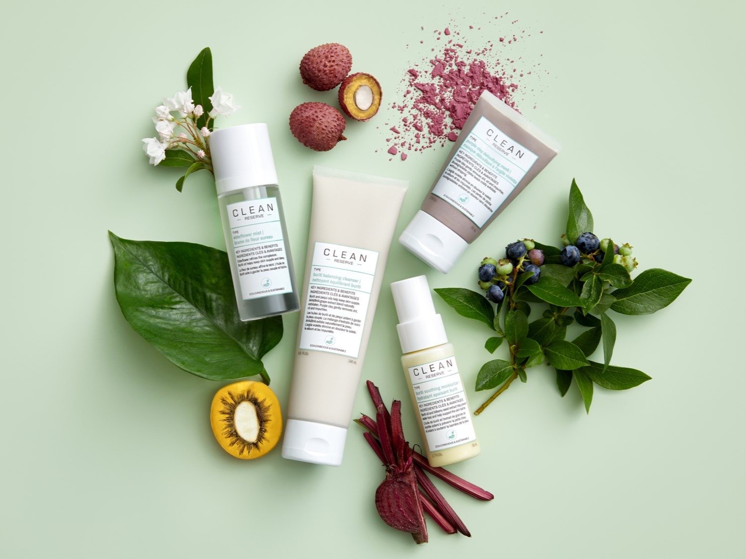 Na jasnozielonym tle leżą produkty do pielęgnacji skóry Clean Reserve, kwiaty, owoce i warzywa, tworząc kompozycję.