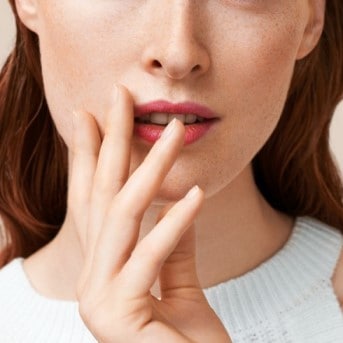 Nahaufnahme einer Frau, die mit einem Finger ihre Lippen berührt, die mit einem rosa Lippenstift geschminkt sind.