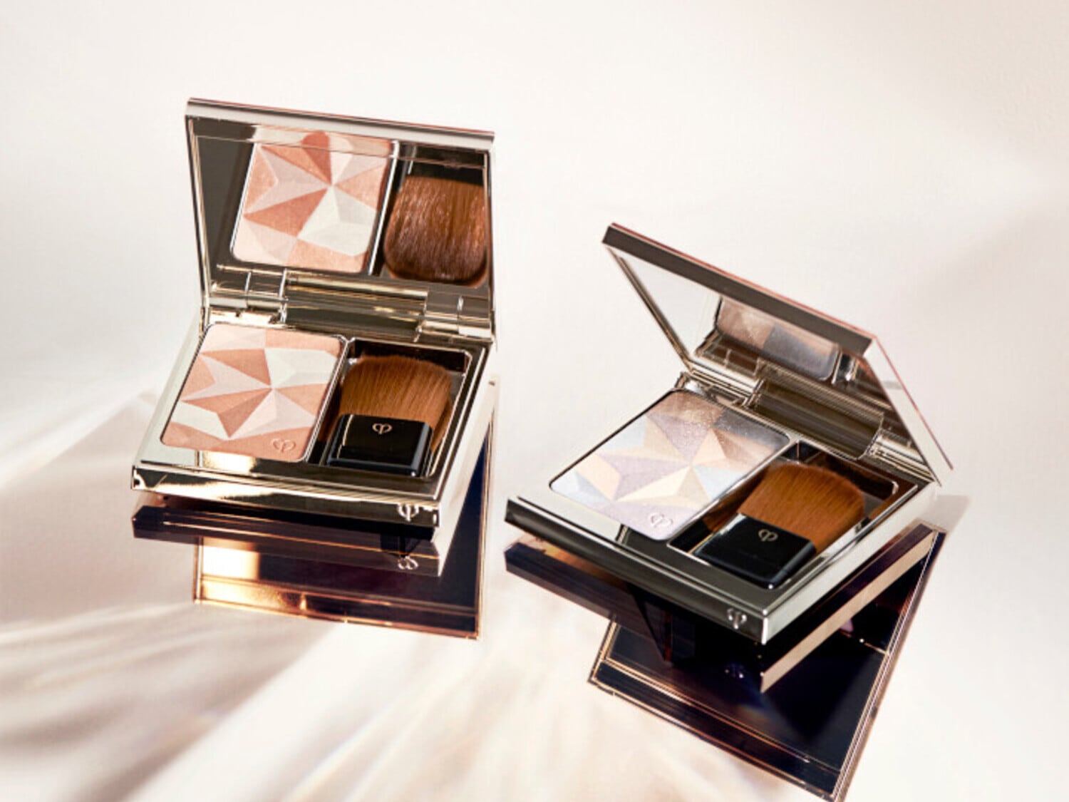 Voici deux poudriers Clé de Peau Beauté ouverts, chacun avec un motif géométrique et un pinceau applicateur, offrant un éclat subtil pour un look sophistiqué.