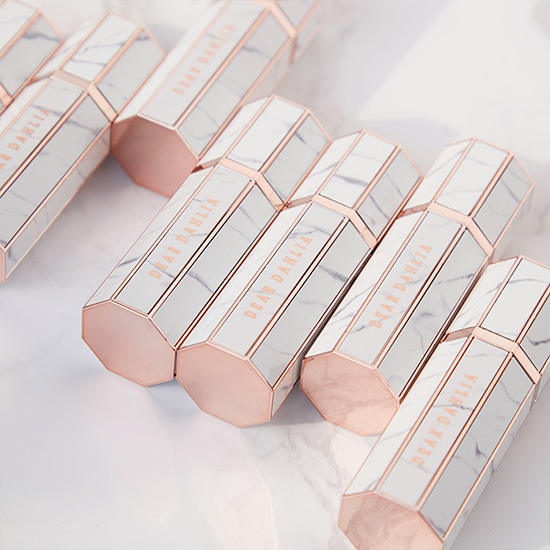 Eleganckie opakowania kosmetyków Dear Dahlia z marmurowym wzorem i różowozłotymi akcentami, ułożone na błyszczącej powierzchni.