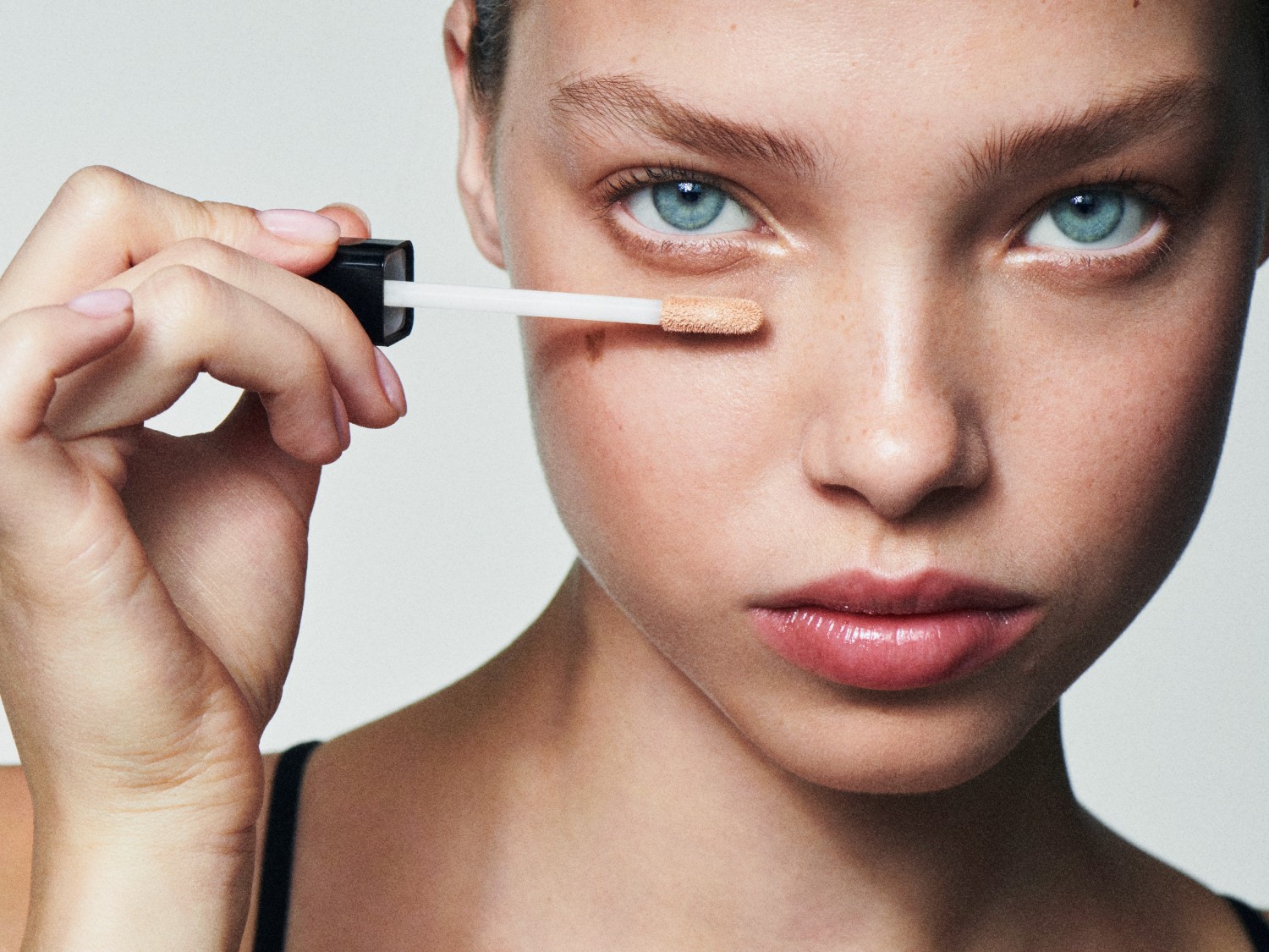 Nahaufnahme einer Frau mit hellblauen Augen, die mit einem Pinsel Concealer unter dem Auge aufträgt, um einen frischen Look zu erzielen.