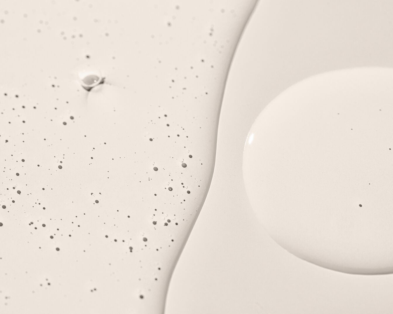 Acercamiento de una textura cremosa de color blanquecino con pequeñas burbujas y gotas, ideal para productos de cuidado de la piel o cosméticos.