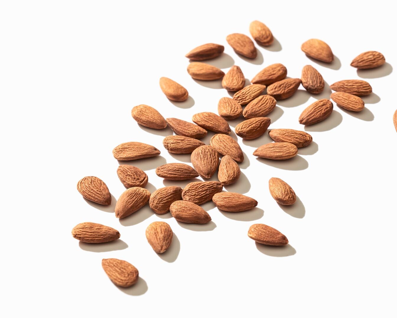 En la imagen se ven varias almendras marrones esparcidas sobre una superficie blanca, creando un patrón visual atractivo y natural.