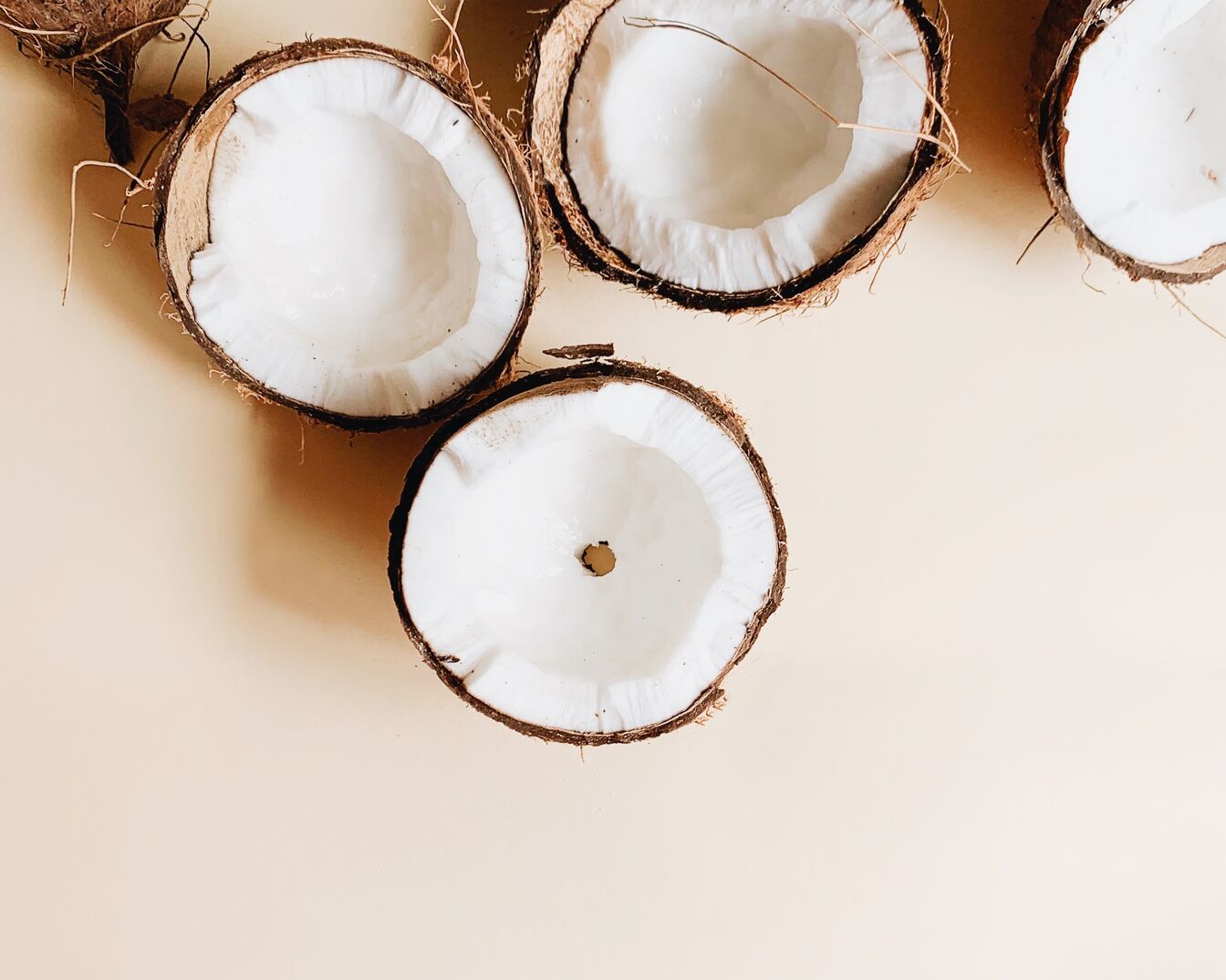 Primer plano de varios cocos partidos por la mitad, mostrando la pulpa blanca y la cáscara marrón, sobre un fondo beige.