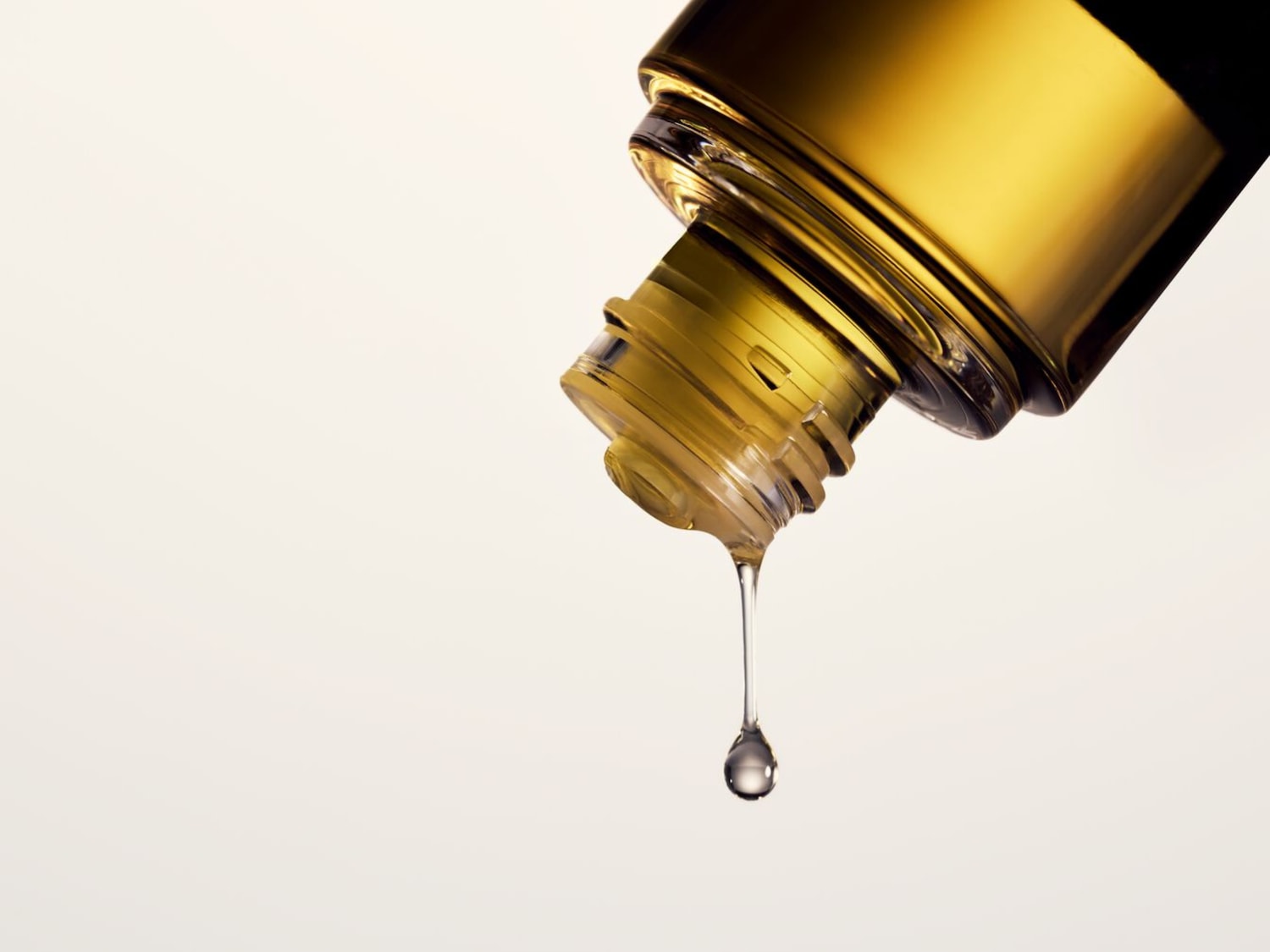 Gouden fles met een druppel olie die eruit valt, wat de essentie en de kwaliteit van het product benadrukt.