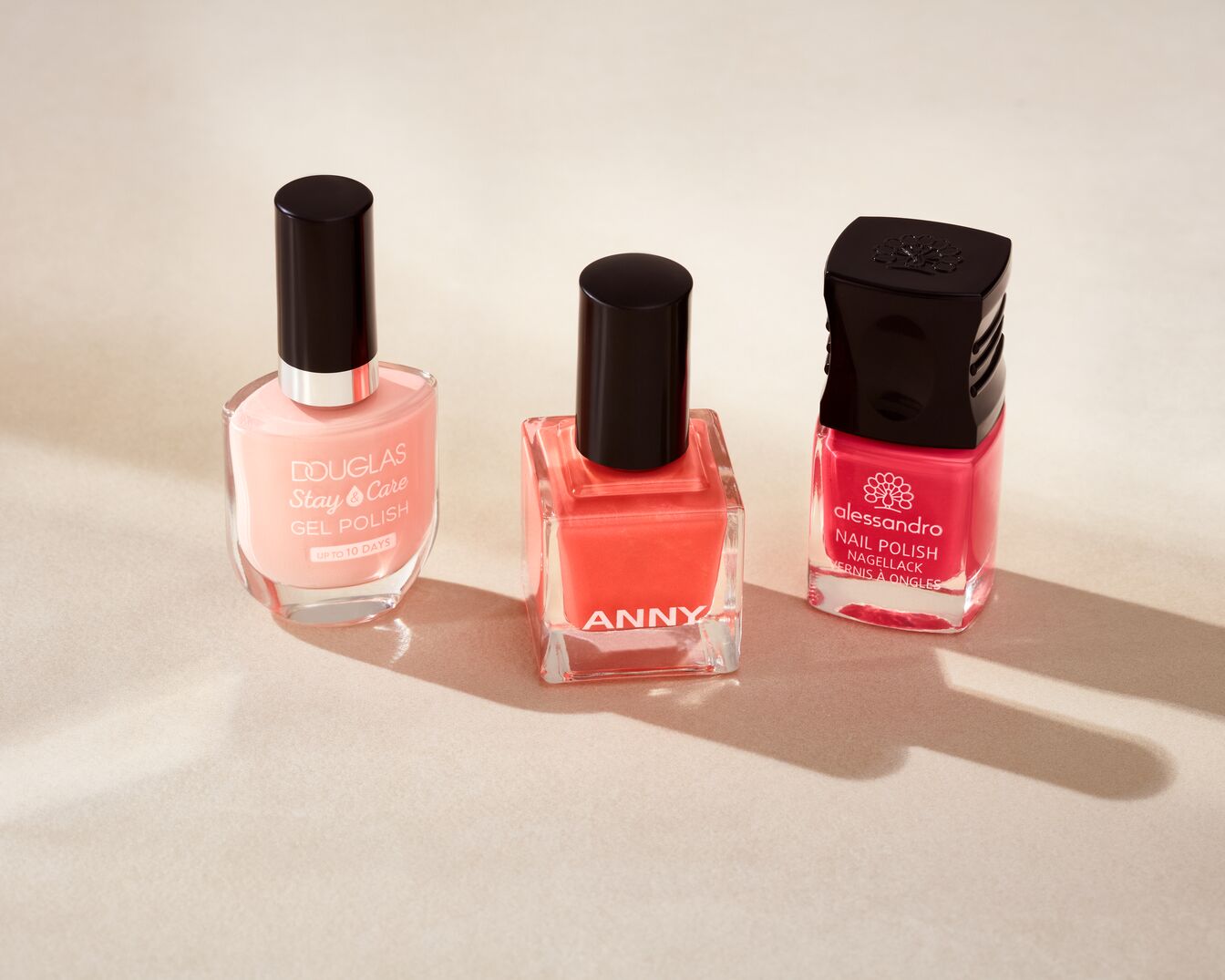 Drei Nagellackflaschen in Rosa-, Korallen- und Rottönen von Douglas, Anny und Alessandro, die eine lebendige Farbpalette für stilvolle Nageldesigns bieten.
