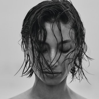Primer plano en blanco y negro de una mujer con el pelo corto y mojado peinado hacia la cara, con los ojos cerrados.