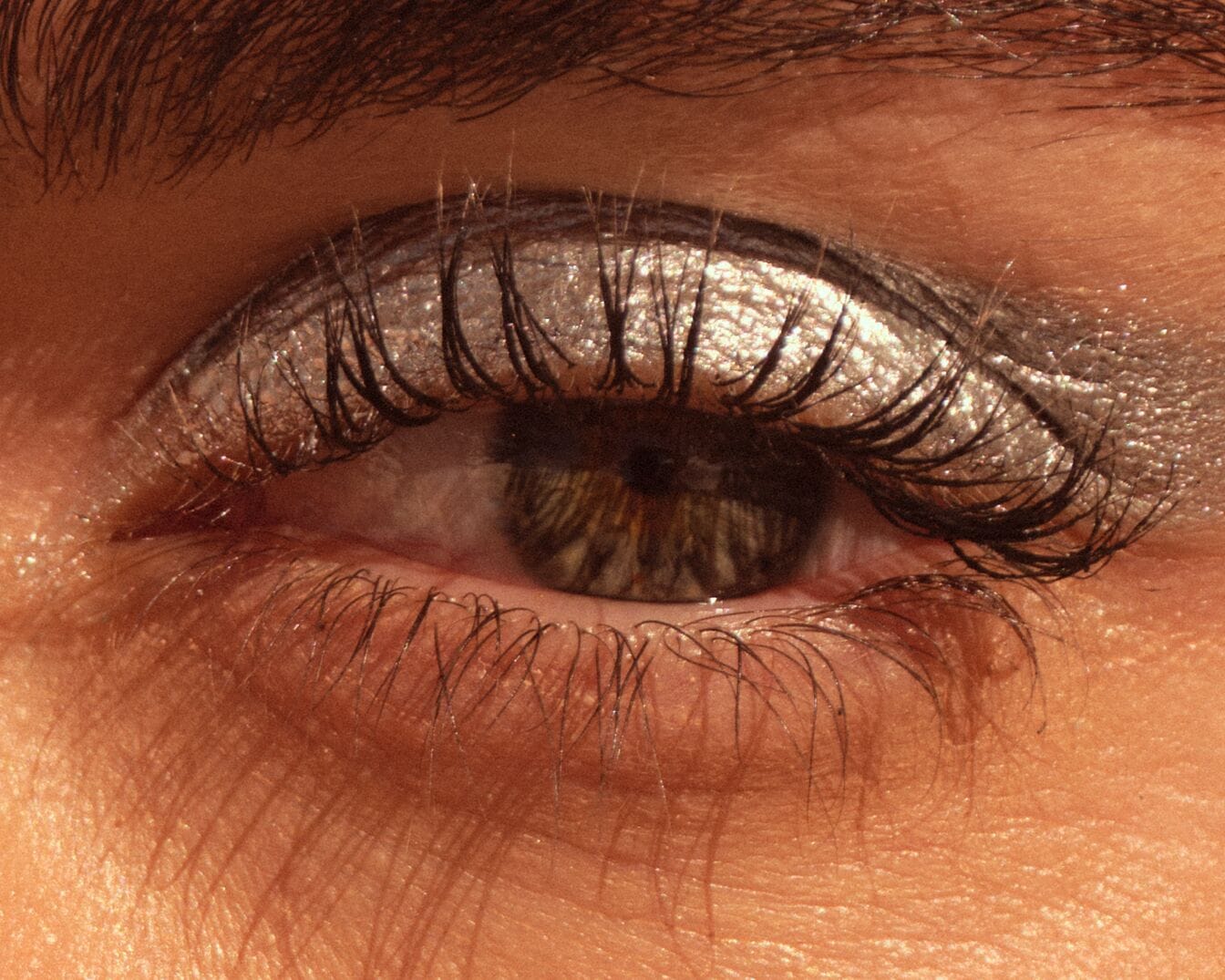 Nahaufnahme eines Auges mit silbernem Glitzer-Lidschatten und dunkler Wimperntusche, die einen glamourösen und auffälligen Look erzeugt.