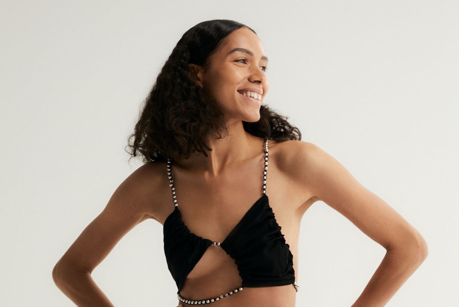 Mosolygó nő fekete, kivágott felsőben, gyöngyökkel díszítve, oldalra nézve, a felsőrészen gyöngyökkel.