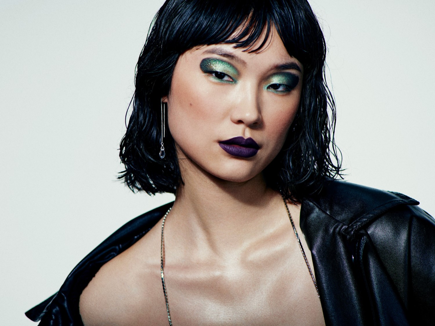 Nahaufnahme einer Frau mit glänzendem, grünem Lidschatten, dunklem Lippenstift und einer schwarzen Lederjacke, die einen modernen und selbstbewussten Look präsentiert.