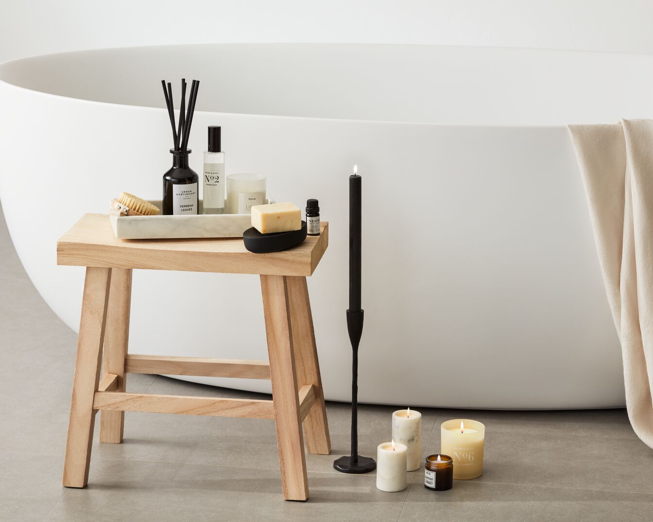 Einrichtung für ein entspannendes Bad mit Kerzen, Duftstäbchen und Badezusätzen auf einem Holzhocker neben einer Badewanne.