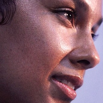 Nahaufnahme eines strahlenden Gesichts mit glänzender Haut und einem sanften Lächeln, das die natürliche Schönheit hervorhebt.