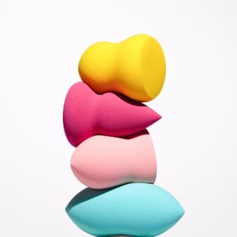 Ein Stapel von vier Make-up-Schwämmen in Gelb, Pink, Rosa und Türkis, die zum Auftragen und Verblenden von Make-up verwendet werden.