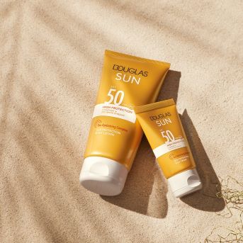 Zwei Tuben Douglas Sun Sonnencreme mit hohem Schutzfaktor 50 liegen auf Sand und bieten optimalen Schutz vor Sonneneinstrahlung.