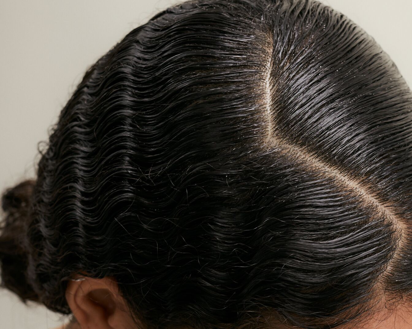 Vista superior del cabello negro peinado en ondas brillantes, mostrando una raya definida y un cuero cabelludo limpio.