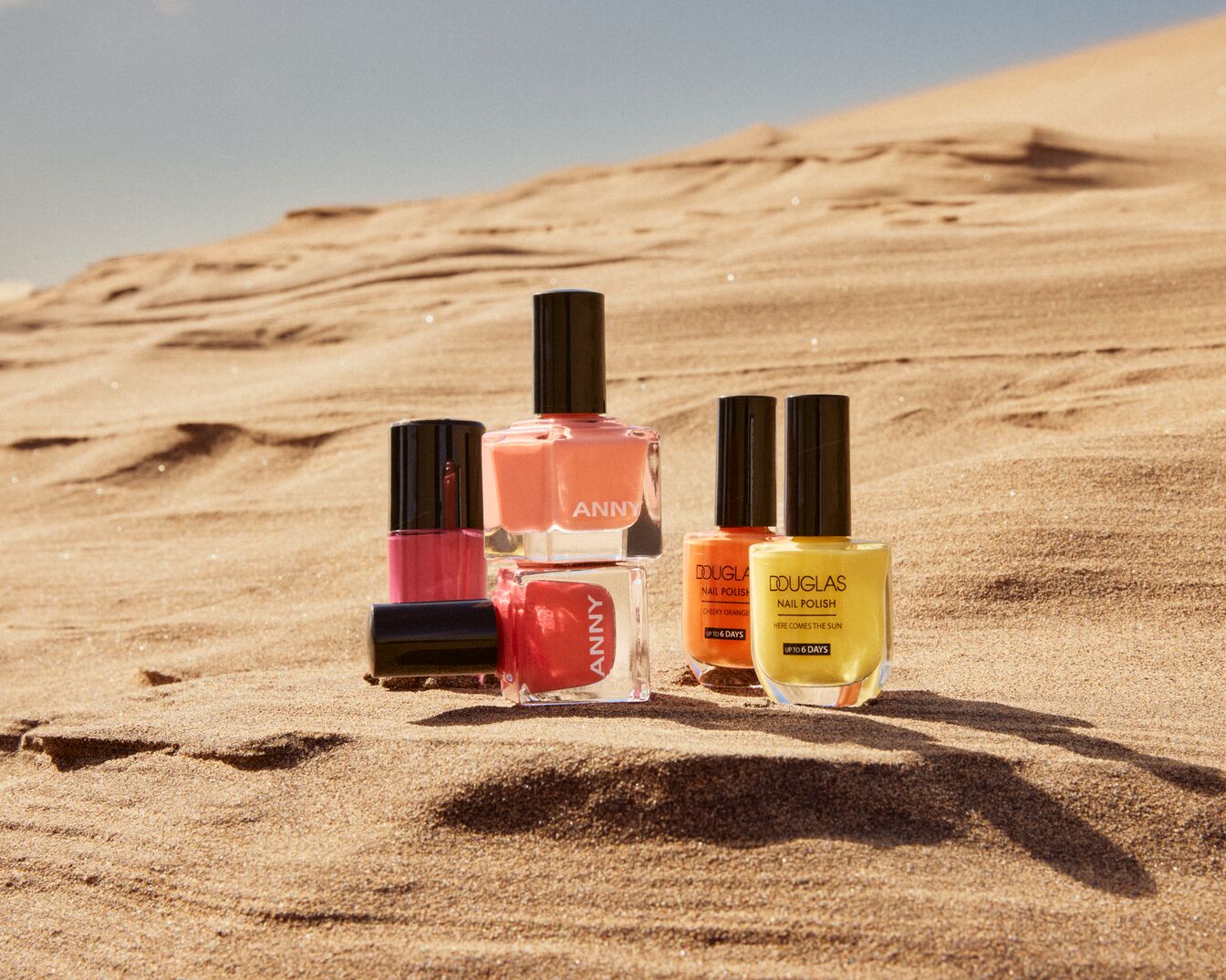 En la arena, esmaltes de uñas de ANNY en tonos rosa, melocotón y rojo, junto con esmaltes de Douglas en naranja y amarillo, prometiendo hasta 6 días de duración.