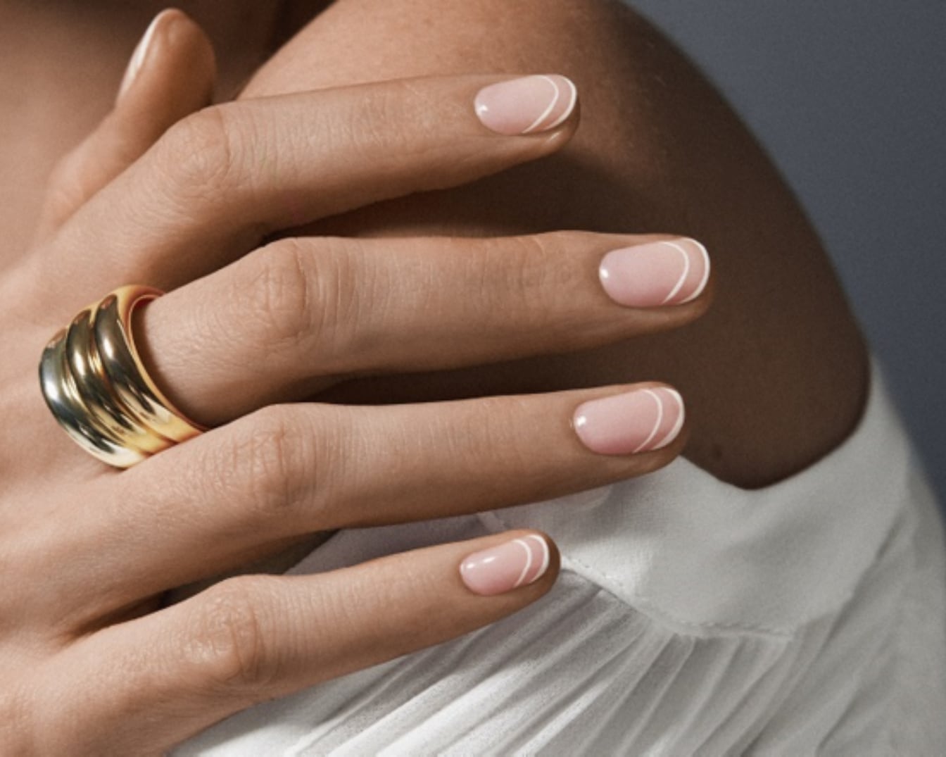 Mano femenina con un anillo dorado y uñas con manicura francesa moderna, con una fina línea blanca que dibuja una media luna en el borde.