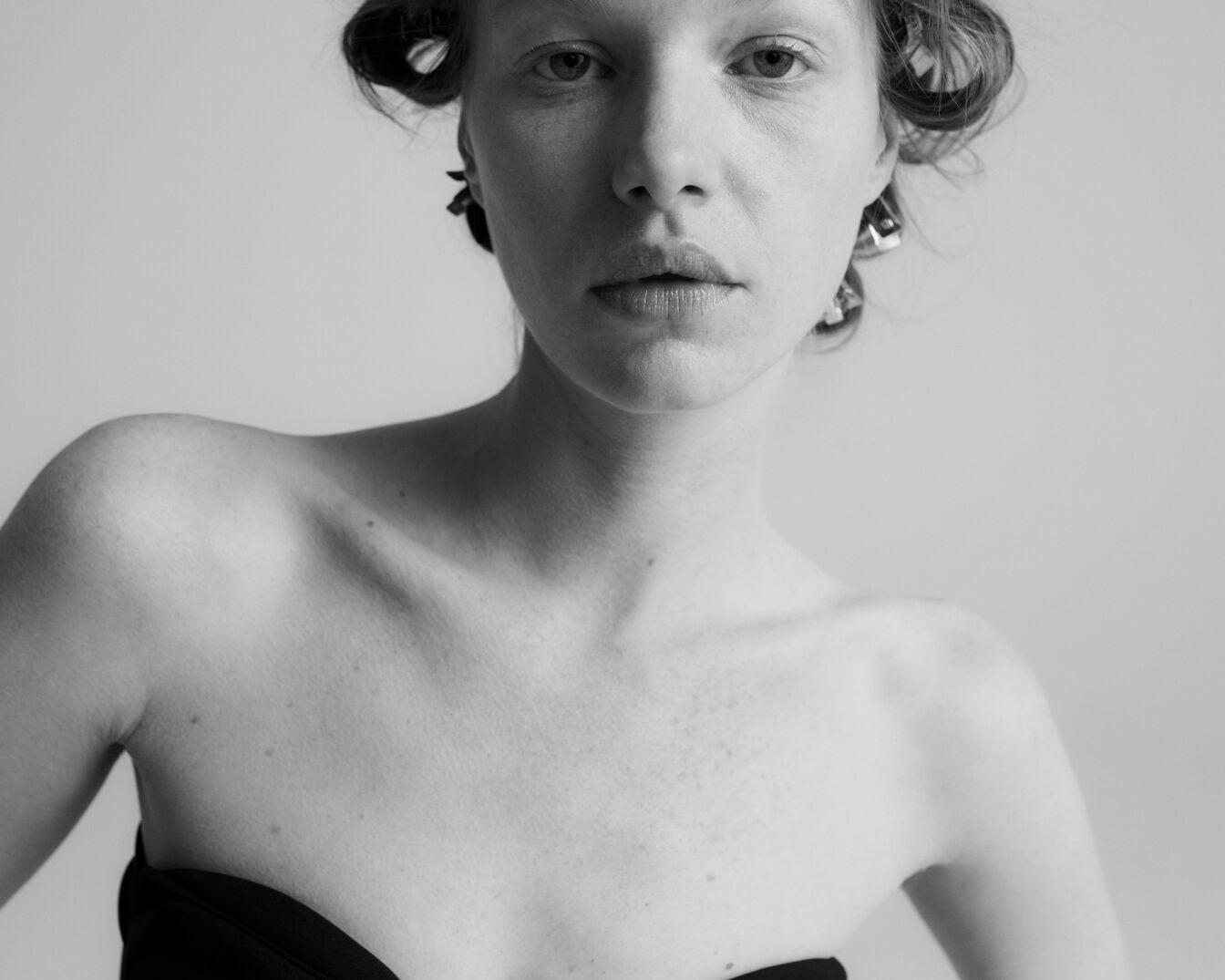 En una imagen en blanco y negro, una mujer de piel clara y hombros descubiertos mira directamente a la cámara con rulos en el pelo.