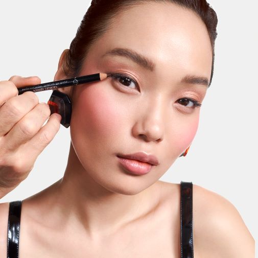 Ein Make-up-Artist trägt mit einem schwarzen Giorgio Armani-Eyeliner einen Lidstrich auf das obere Augenlid eines asiatischen Models auf.