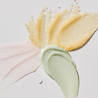 Verschillende texturen en kleuren van huidverzorgingsproducten, waaronder roze, geel en groen, op een witte achtergrond.