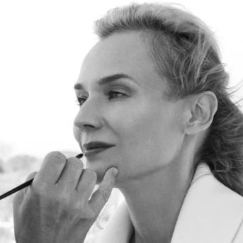 En esta imagen en blanco y negro, una maquilladora aplica cuidadosamente lápiz labial a una mujer de mediana edad, resaltando sus rasgos con precisión.