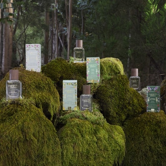 Esplora Jardin Bohème, una collezione di profumi presentata su un letto di muschio verde, con flaconi trasparenti e confezioni decorate con motivi floreali.