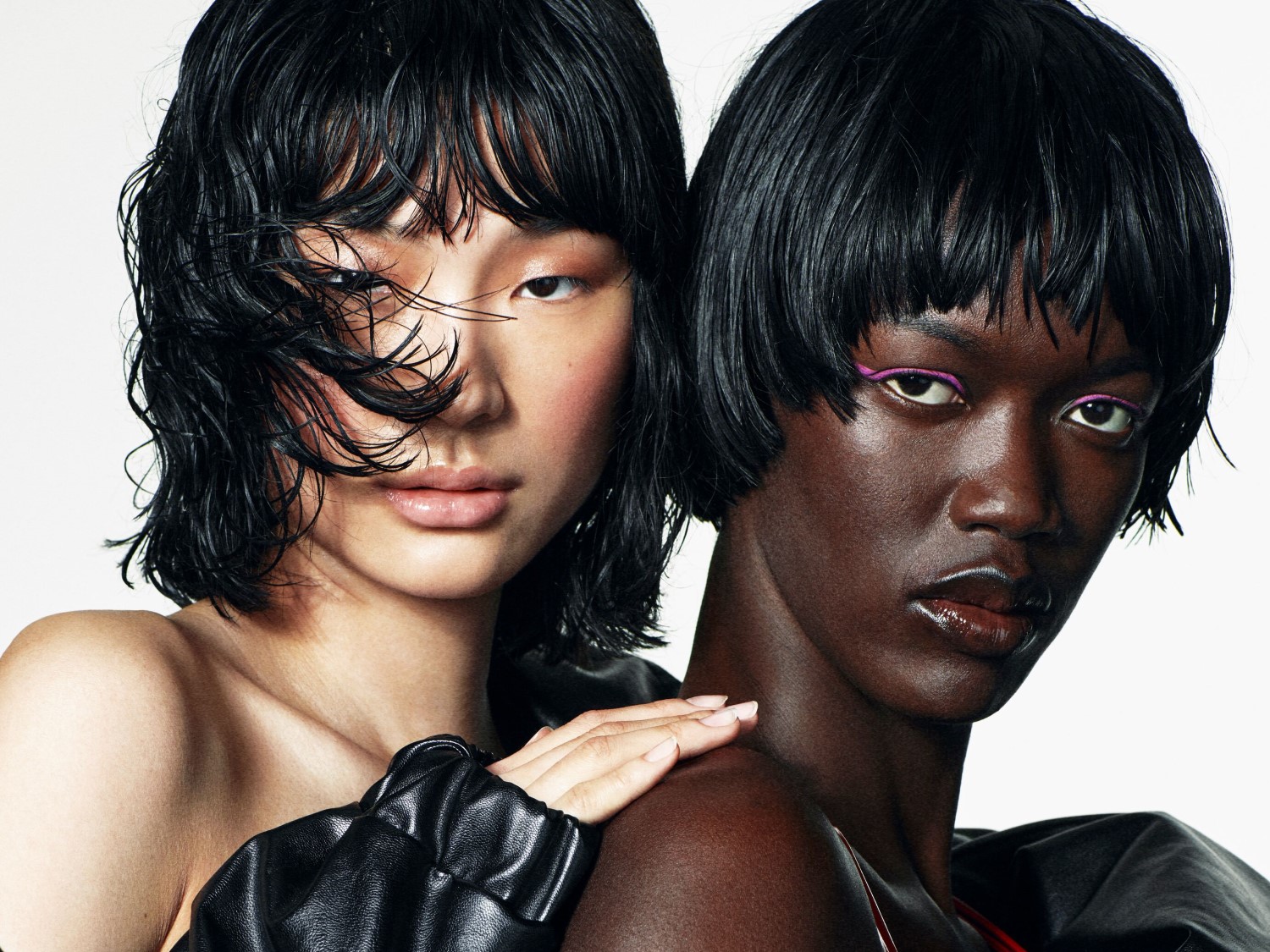 Zwei Models mit glänzenden, dunklen Bob-Frisuren und natürlichem Make-up, wobei das eine Model einen Hauch von pinkfarbenem Eyeliner trägt, posieren eng beieinander.