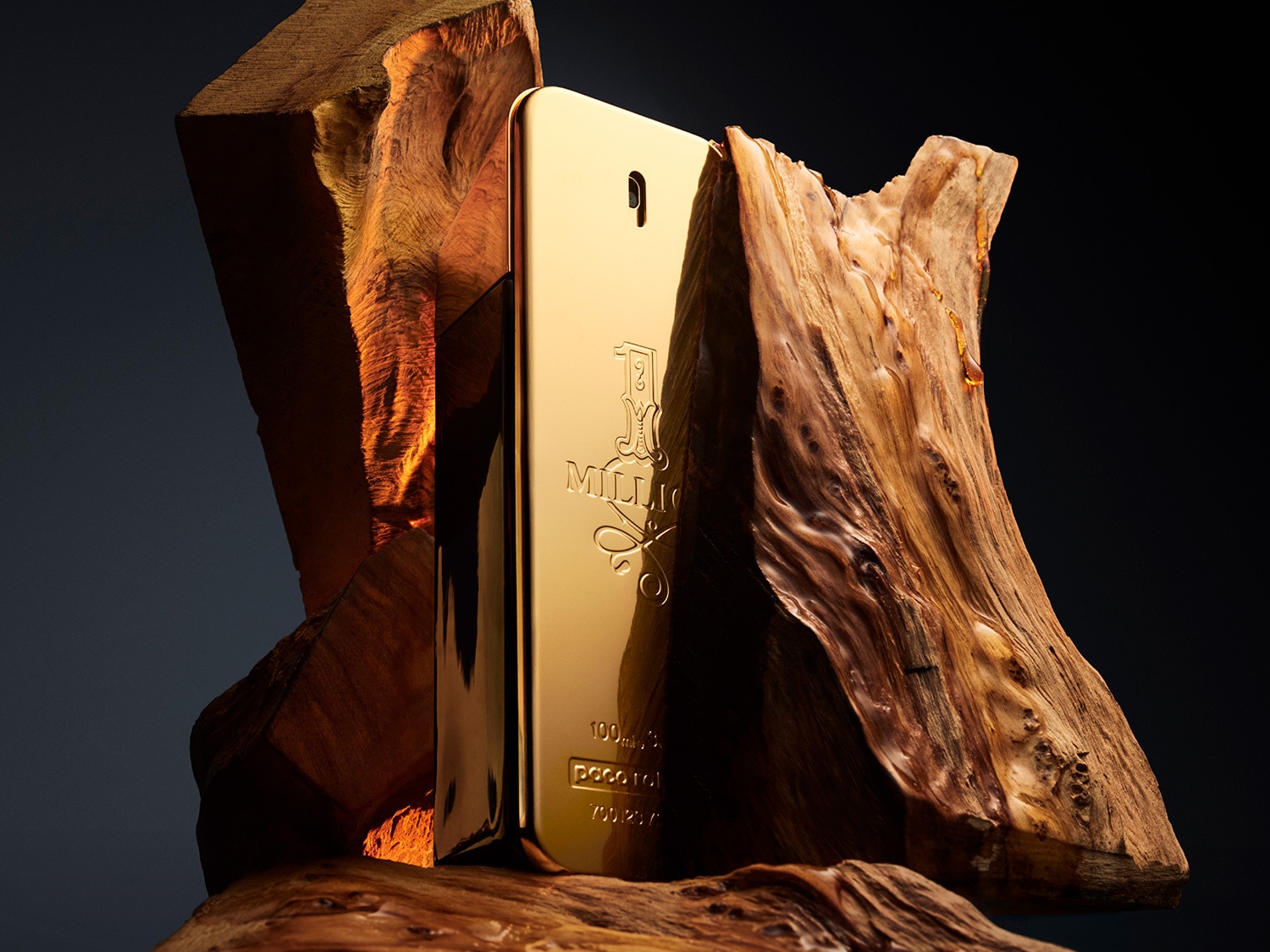 El perfume 1 Million de Paco Rabanne, con su envase dorado que evoca un lingote de oro, se presenta entre trozos de madera rústica, combinando lujo y naturaleza.