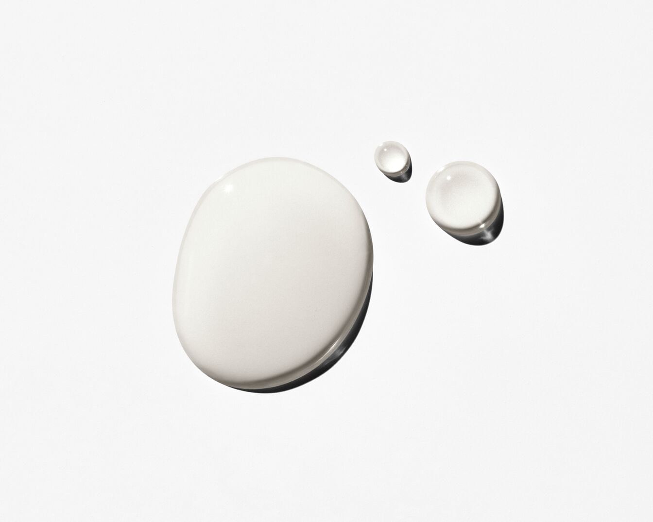 Gotas de suero blanco lechoso sobre una superficie blanca, que muestran la textura hidratante y suave del producto.