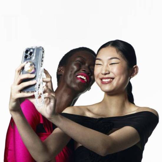 Dwie uśmiechnięte kobiety robią sobie selfie telefonem w przezroczystym etui z uchwytem.