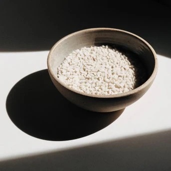 Un cuenco de cerámica lleno de pequeñas piedras blancas, iluminado por una luz brillante que proyecta una sombra oscura, ideal para la meditación o la decoración zen.