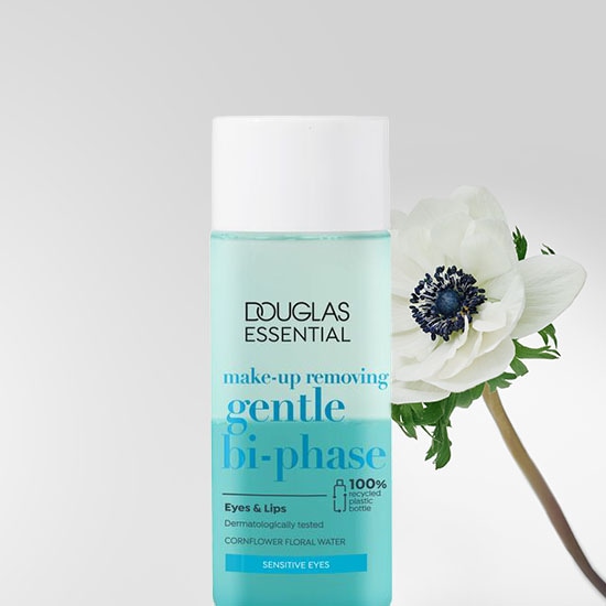 Płyn do demakijażu Douglas Essential Gentle Bi-Phase w przezroczystej butelce z białą nakrętką, ozdobiony białym kwiatem, idealny do oczu i ust, testowany dermatologicznie, zawiera wodę kwiatową z bławatka i jest przeznaczony do wrażliwych oczu.