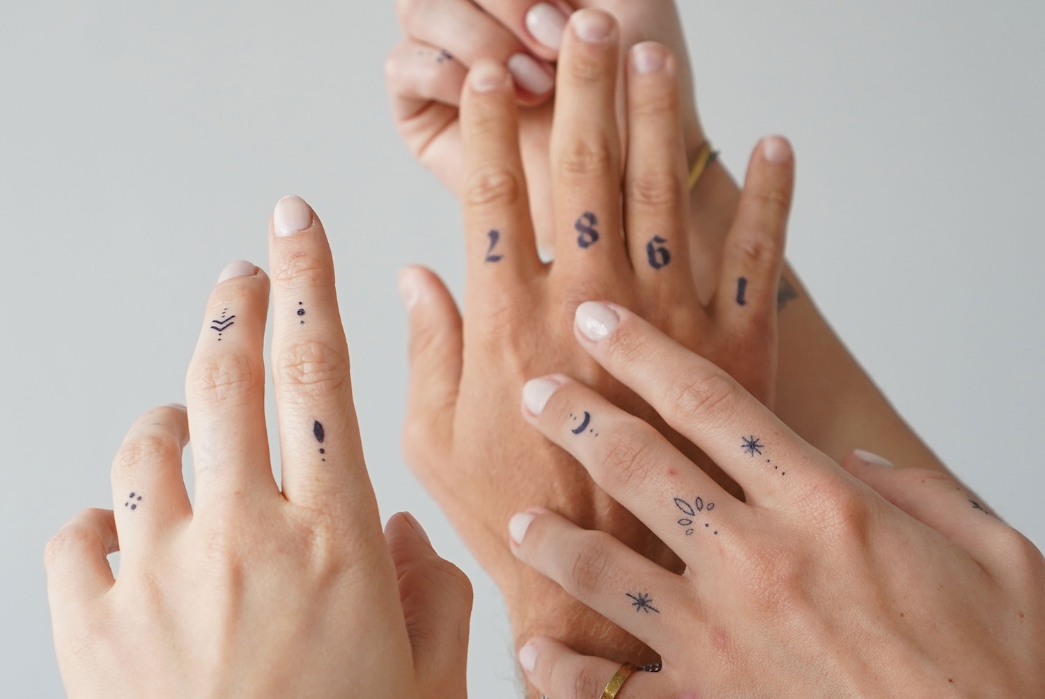 Nahaufnahme von Händen mit temporären Tattoos, darunter geometrische Formen, Zahlen und Sterne.