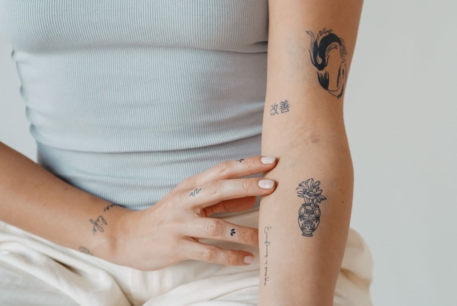 Nahaufnahme einer Frau mit verschiedenen Tätowierungen auf ihrem Arm, darunter ein Fisch, chinesische Schriftzeichen und eine Vase mit Blumen.