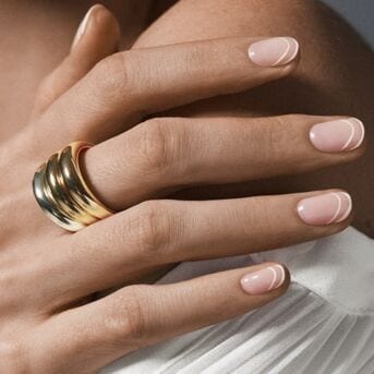 Nahaufnahme einer Hand mit einem goldenen Ring und hellrosa lackierten Nägeln mit weißen Linien.