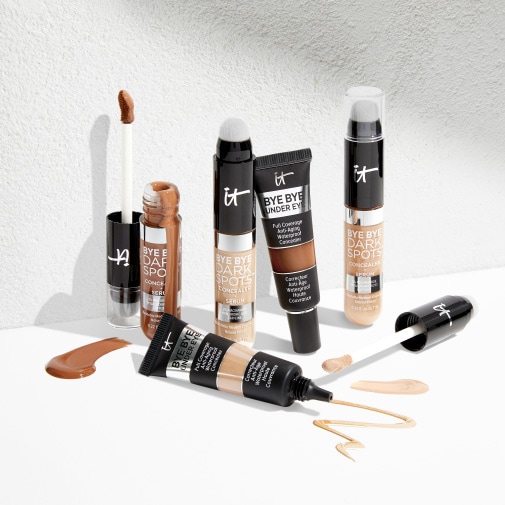 Eine Auswahl an IT Cosmetics Concealern in verschiedenen Farbtönen und Texturen, darunter Tuben und Applikatoren, die für eine vollständige Abdeckung von Augenringen und dunklen Flecken sorgen.