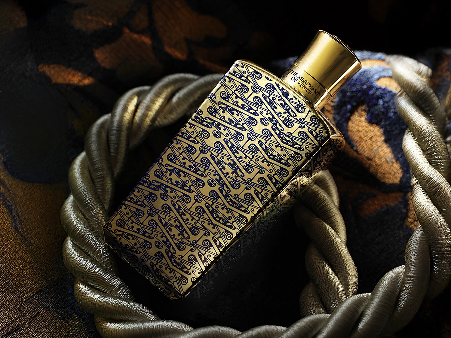 Butelka perfum The Merchant of Venice w złotym kolorze z niebieskimi wzorami, umieszczona w ozdobnym, plecionym sznurze.