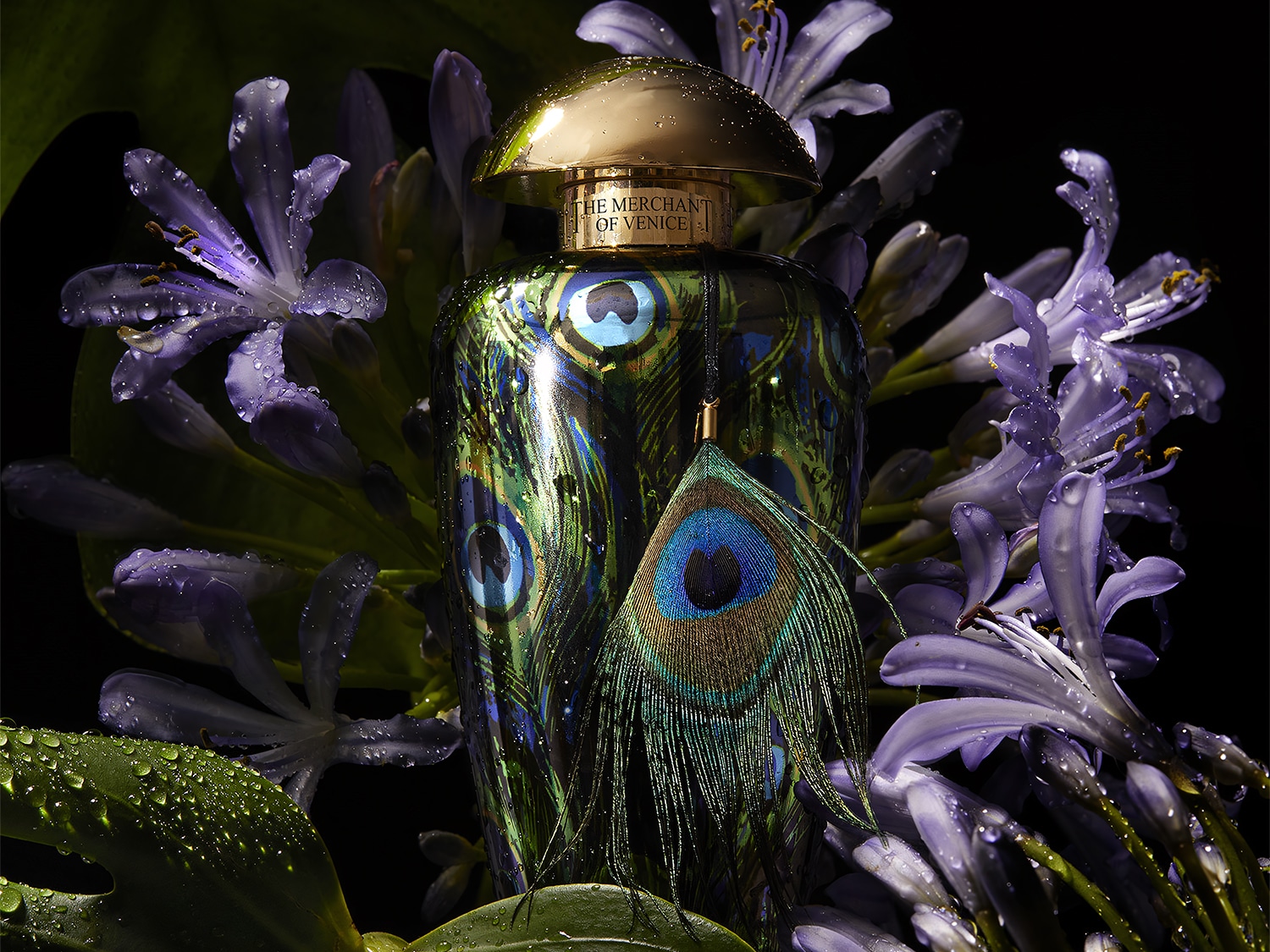 Butelka perfum The Merchant of Venice z motywem pawich piór, otoczona fioletowymi kwiatami i zielonymi liśćmi, tworzy bogatą i egzotyczną kompozycję.