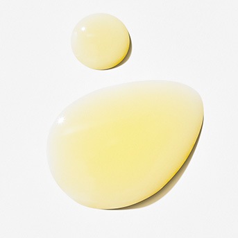 Gocce di siero giallo chiaro su una superficie bianca, che mostrano la consistenza liscia e idratante del prodotto.