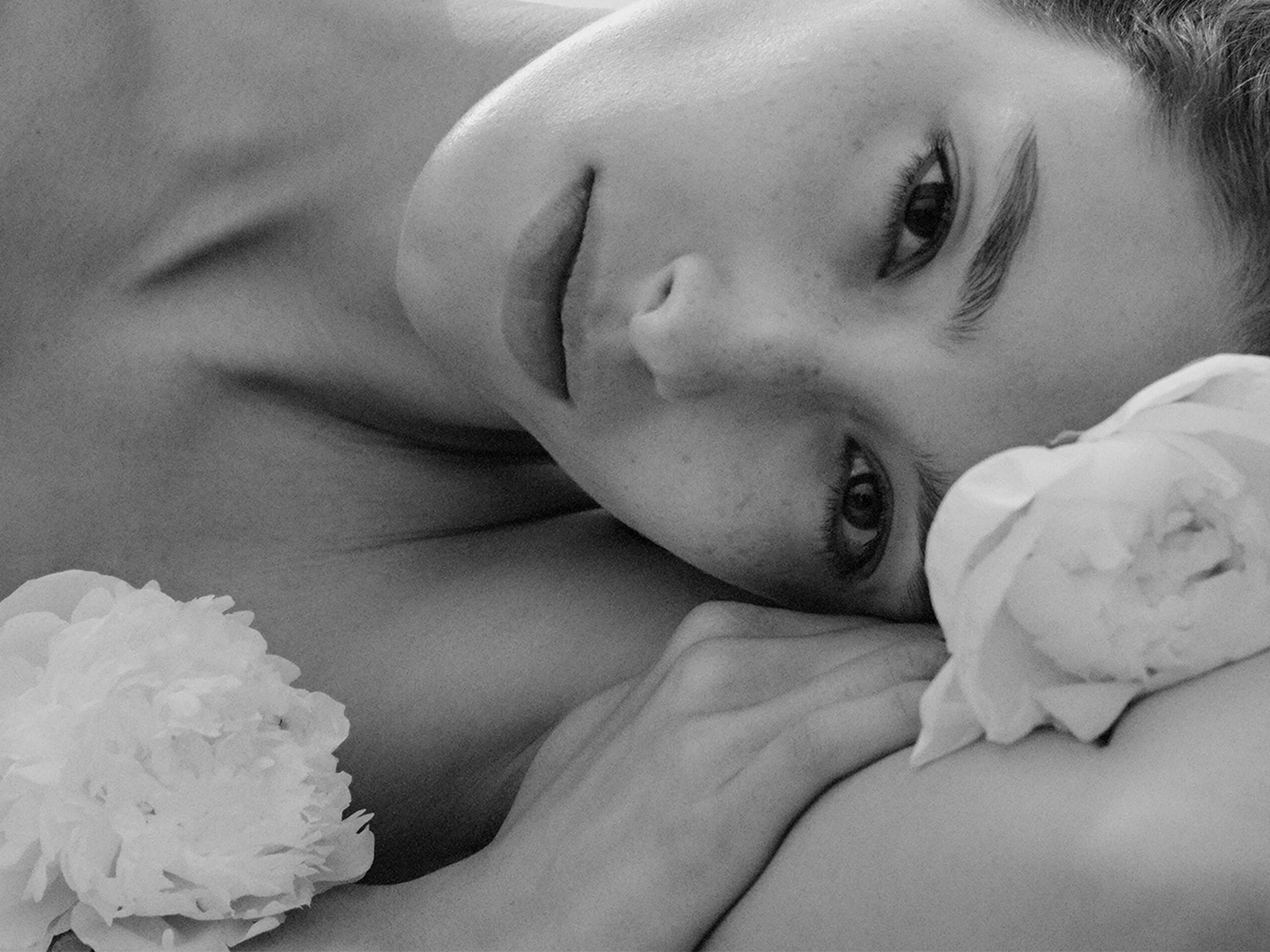 Primo piano in bianco e nero di una donna che riposa con dei fiori bianchi, che mostra un'espressione serena e rilassata.