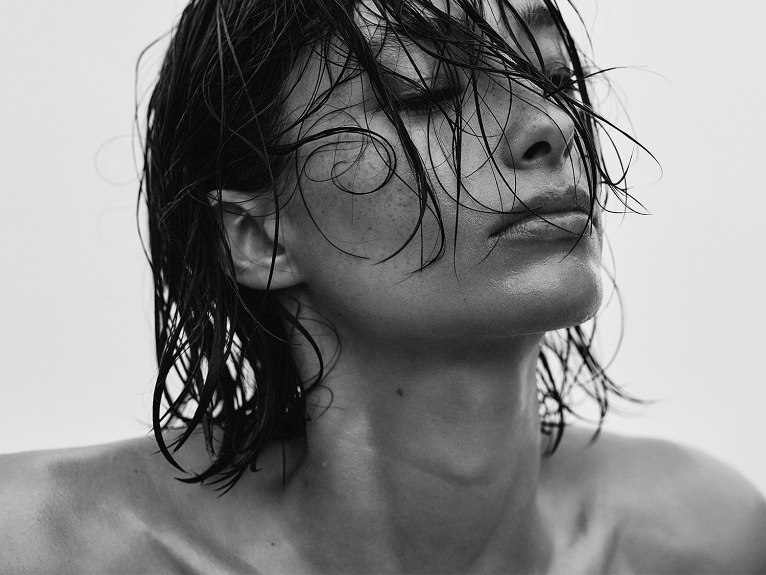 Primo piano in bianco e nero di una donna con i capelli bagnati che le ricadono sul viso, creando un look fresco e naturale.