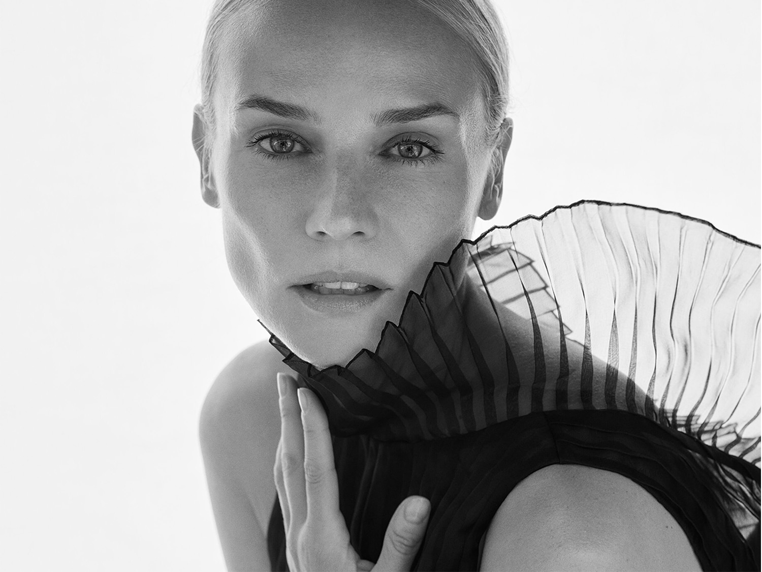 Primo piano in bianco e nero di una donna con un abito nero plissettato con volant che le incornicia il viso, creando un look elegante e sofisticato.