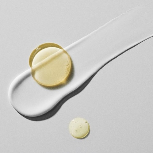 Nahaufnahme von Hautpflegeprodukten, darunter ein gelbes Ölserum und eine weiße Creme, die auf einer ebenen Fläche verteilt sind.