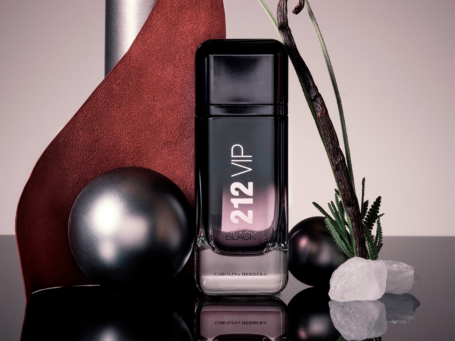El frasco de perfume 212 VIP Black de Carolina Herrera, en tonos negros degradados a transparente, destaca con elegancia entre elementos decorativos como esferas y texturas.