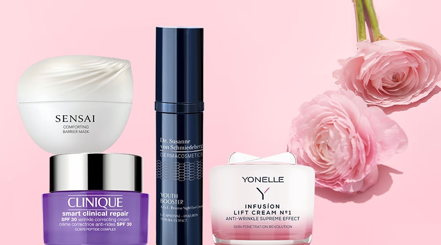 Różne kremy do twarzy marek Sensai, Clinique, Dr. Susanne von Schmiedeberg i Yonelle na różowym tle z kwiatami.